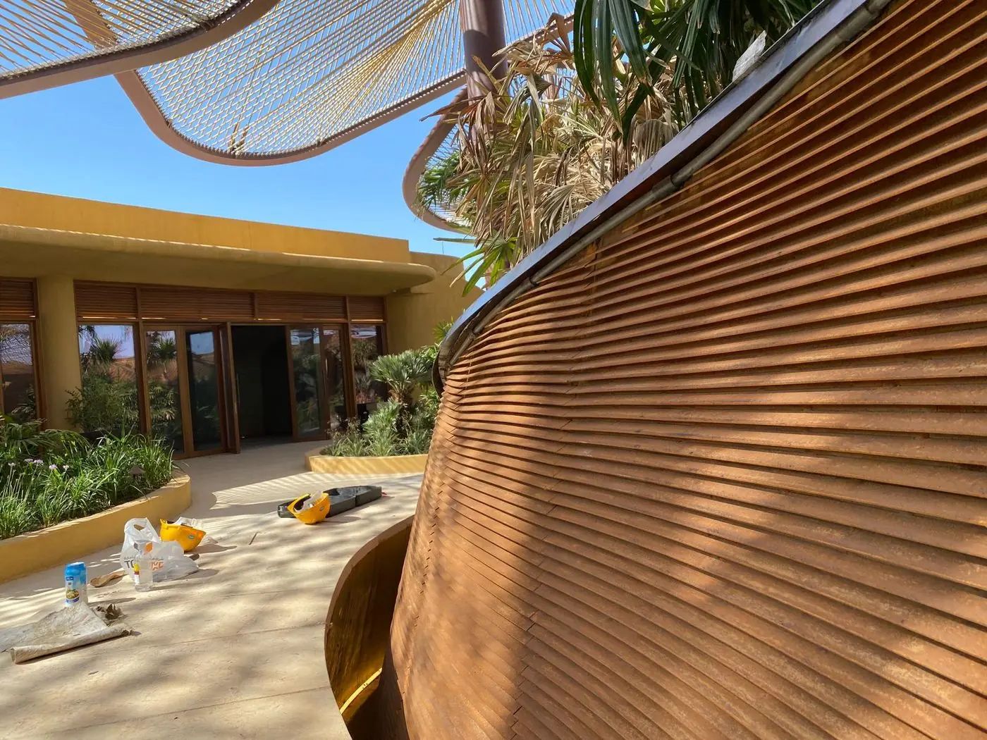 A Cor-Ten fin screen curving around a pavilion, its weathered face catching low sun.